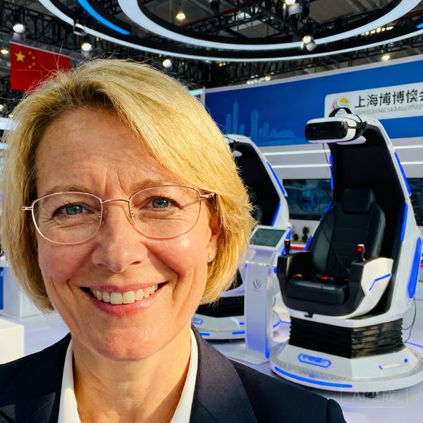 德国制造企业亚太区市场总监Mueller女士的职业肖像，她留着金色短发，佩戴细框眼镜，站在上海进博会展厅的VR体验区前微笑。